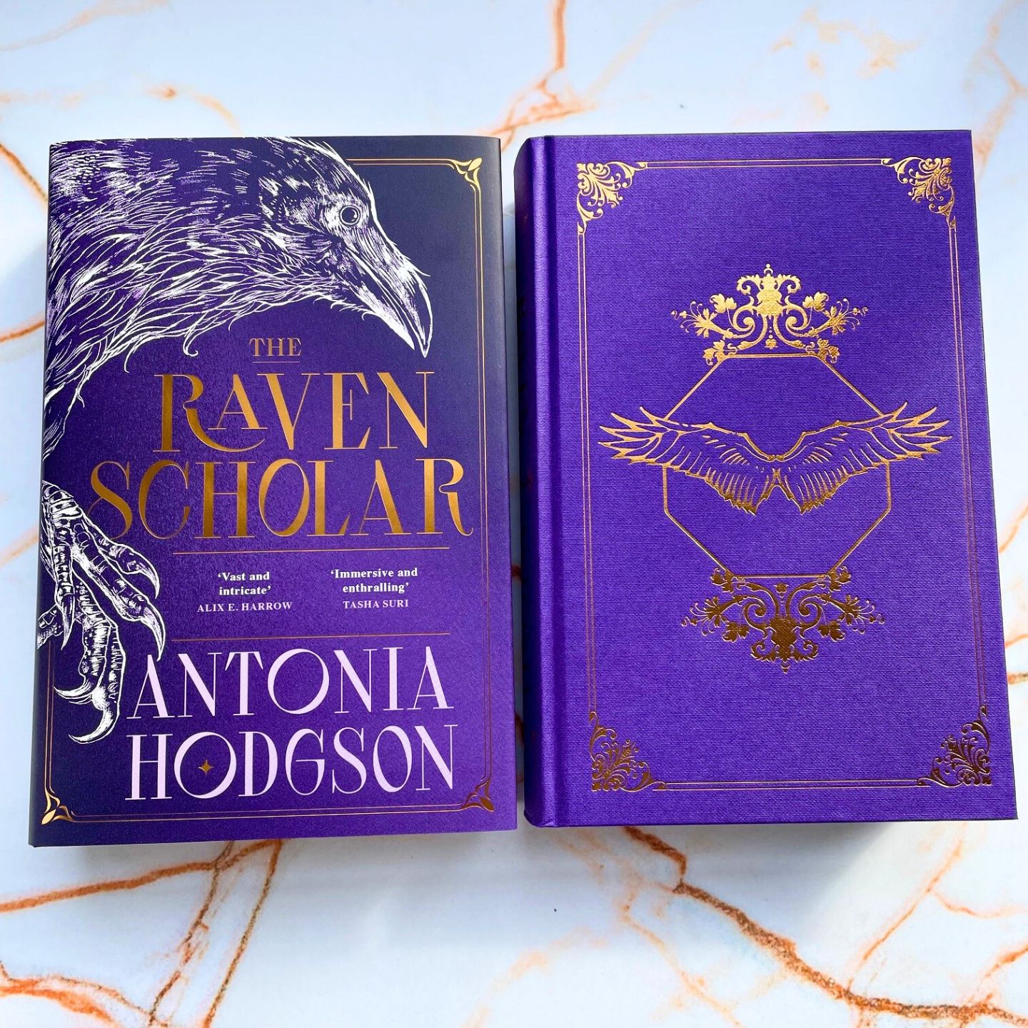 photo of Raven scholar book, purple with white line drawing of a raven. Title in gold foil. Image of under cover boards, purple with gold foil image of Raven sigil - octagon with Raven wings